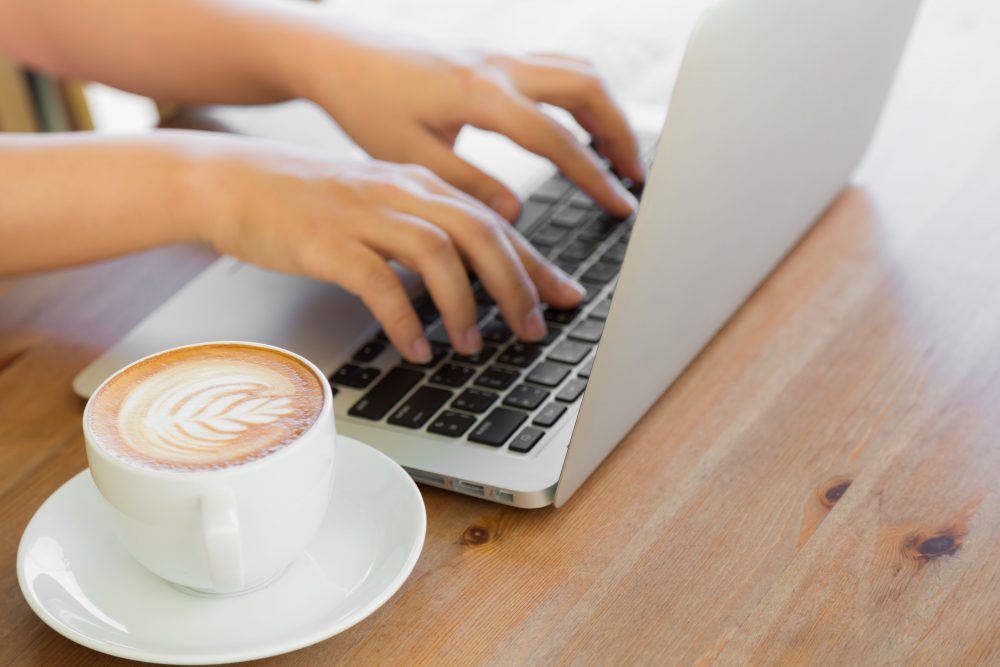 Closeup of business woman hand typing on laptop keyboard and coffee